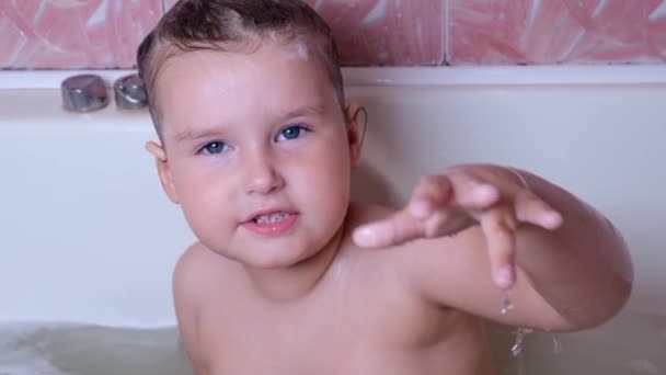 Malá vtipná dívka 3 roky staré koupele a myje se s pěnou na hlavě ve vodě v koupelně doma. Koncept péče o dítě, hygiena. — Stock video