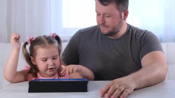 Niña de 3 años dibuja con su padre y ve una lección de dibujo en línea en una tableta en casa. El concepto de la enseñanza a distancia en línea escuela — Vídeo de stock