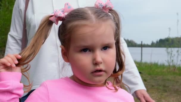 Retrato de una linda niña de 3 años, vestida con una sudadera rosa con dos colas de caballo, jugando al aire libre en la naturaleza. Concepto de infancia feliz, desarrollo infantil — Vídeos de Stock