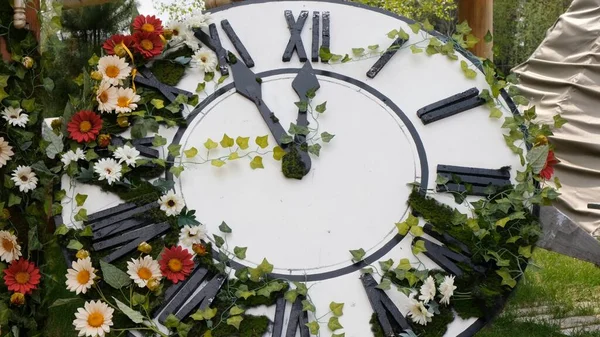 Relógio de parede grande no campo em flores florescendo, mostrando o tempo 11: 55, 12: 00. conceito de gerenciamento de tempo, horário de verão. Primavera ou casamento. Piquenique de dia de mulheres — Fotografia de Stock