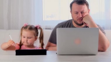 Sıkılmış bir iş adamının babası evde dizüstü bilgisayarda çalışıyor. Yanında 3 yaşında bir kız var. Tablette oynuyor. Modern aile. Serbest meslek kavramı. Aygıtlara bağımlılık