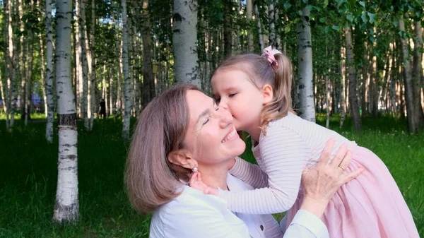 Cute granddaughter, 3 years old, tells her happy smiling grandmother a secret in her ear. The concept of a happy relationship between generations, raising children — Stock Photo, Image