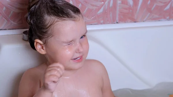 Klein meisje 3 jaar oud baadt en wast in de badkamer thuis, water komt in de ogen van het kind tijdens het baden, huilen. Baby lichaamsverzorging concept, hygiëne. — Stockfoto