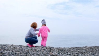 Büyükanne ve torun kıyı boyunca yürür, oynar, taş atar ve sonbahar günü eğlenirler. Çocukluk kavramı, ebeveynlik, çocuklar ve ebeveynler arasındaki ilişkiler