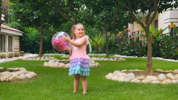 快乐的小女孩，3岁，头上顶着两条马尾辫，穿着一件淡淡的、五颜六色的粉色蓝色连衣裙，玩着一个色彩斑斓的透明球，头戴多彩的羽毛 — 图库照片