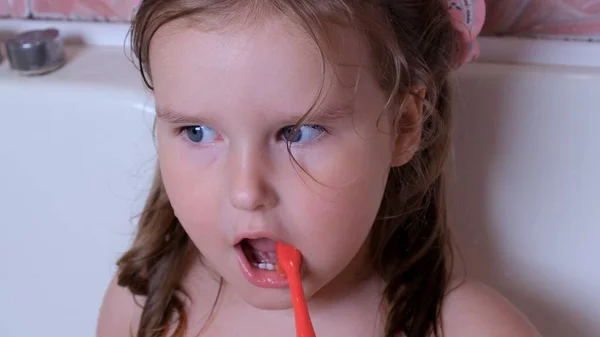 Pequena menina bonita 3 anos escova os dentes com uma escova de dentes vermelha no banheiro em casa. Saúde, higiene dentária, pessoas e conceito de beleza — Fotografia de Stock