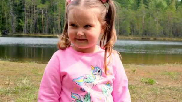 핑크 색 스웨트 셔츠를 입고 두 머리가 달린 3 살난귀여운 여자 아이의 초상화가 자연스럽게 야외에서 놀고 있다. 행복 한 어린 시절의 개념, 아이들의 발달 — 비디오