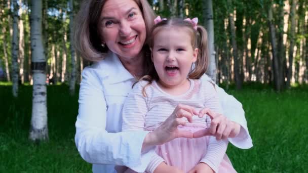 Nevető nagymama és unokája, 3 éves, mutassa meg a szívét a kezükből. A generációk közötti boldog kapcsolat fogalma, a gyermeknevelés — Stock videók