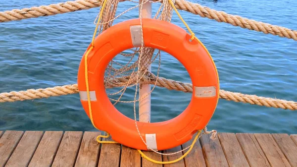 Linha de vida laranja e cordas do mar no fundo do mar e céu azul. Cordas marinhas e salva-vidas pendurados num poste. Conceito de ajuda e segurança — Fotografia de Stock
