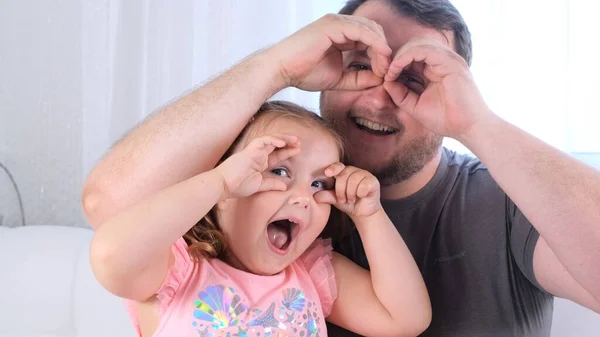 Engraçada Filhinha de 3 anos e pai estão se divertindo em casa, fazendo caras engraçadas, fazendo óculos com os dedos, como óculos olhando para a câmera através de binóculos. divirta-se com criança — Fotografia de Stock