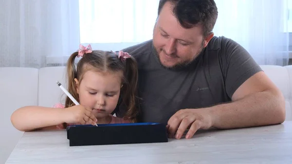 3 살짜리 여자 아이와 아빠가 태블릿으로 그림을 그리고 집에서 온라인으로 그림 수업을 보고 있습니다. 아버지는 딸들 이성공한 것을 기뻐하며 딸 이연구할 때 도움을 줍니다. 온라인 학교의 거리 — 스톡 사진