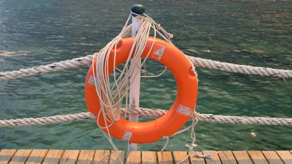 Linha de vida laranja e cordas do mar no fundo do mar e céu azul. Cordas marinhas e salva-vidas pendurados num poste. Conceito de ajuda e segurança — Fotografia de Stock