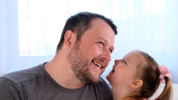 Little joyful daughter, 3 years old, tells her dad a secret, play together at home. Fathers day. Handsome young man at home with his little cute girl are having fun together. Fatherhood concept — Stock Photo, Image