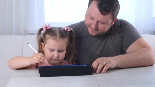 Klein meisje 3 jaar oud en haar vader tekenen op de tablet en thuis kijken naar een tekenles online. Papa verheugt zich over het succes van zijn dochters en helpt haar bij haar studie. Online schoolafstand — Stockvideo