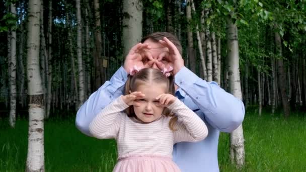 Cute family, father, adorable daughter sitting on the street, making funny faces, making glasses shape with fingers, like glasses looking through binoculars, have fun with child, free time, tricks — Stock Video