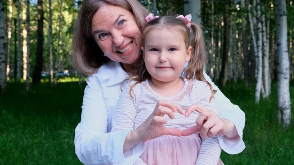 Nonna e nipote ridenti, 3 anni, mostrano il cuore fuori dalle loro mani. Il concetto di un felice rapporto tra generazioni, crescere i figli — Foto Stock