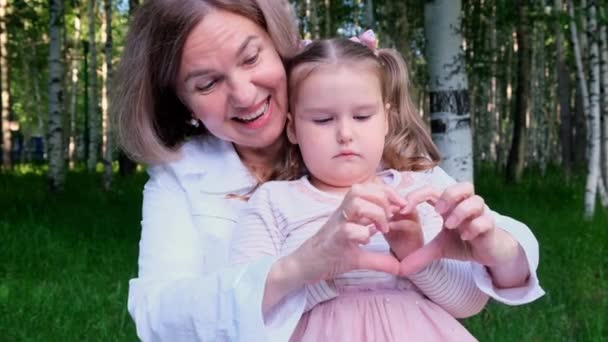 幸せな愛情の祖母と孫娘、 3歳、彼らの手から彼らの心を示しています。世代間の幸せな関係の概念は、子供を育てる — ストック動画