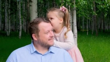 Şirin küçük bir kız, 3 yaşında, babasının kulağına söyler ve güler. Mutlu bir çocukluk, babalık, ebeveynlik kavramı. Ebeveynler ve çocuklar arasındaki güven ilişkisi. Babalar Günü