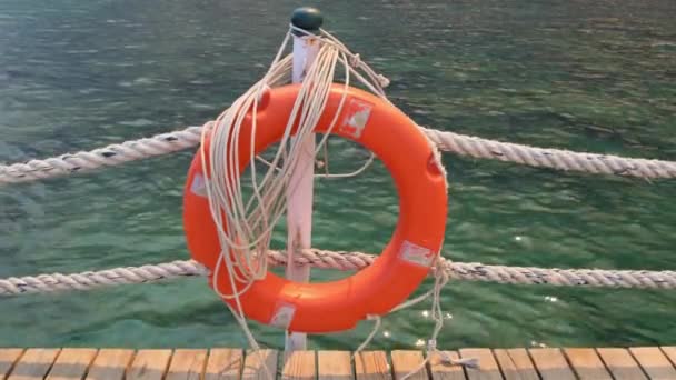 Orange lifeline and sea ropes on the background of the sea and blue sky. Marine ropes and life preserver hanging on a post. Help and safety concept — Stock Video