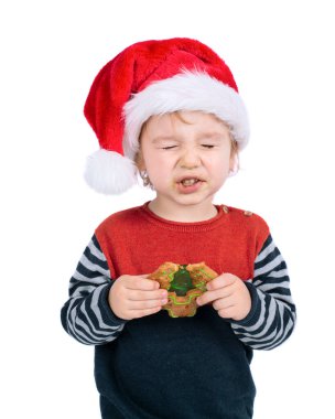 Noel Baba şapkalı küçük çocuk beyaz arka planda izole edilmiş Noel çöreği yiyor.