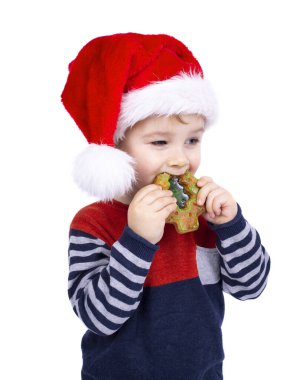 Noel Baba şapkalı küçük çocuk beyaz arka planda izole edilmiş Noel çöreği yiyor.