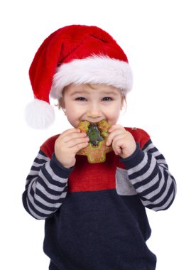 Noel Baba şapkalı küçük çocuk beyaz arka planda izole edilmiş Noel çöreği yiyor.