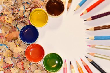 Masanın üzerinde sivri renkli kalemler, tahta talaşları ve suluboya boya kavanozları yatıyor. Yüksek kalite fotoğraf