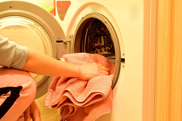 Young woman lays dirty laundry for washing in the drum of the washing machine.