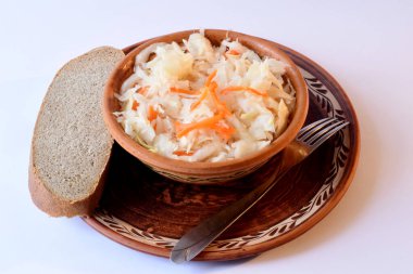 Kırmızı havuçlu hazır lahana turşusu, beyaz bir masanın yüzeyine yerleştirilmiş seramik bir tabağa konur.