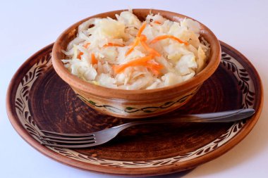 Kırmızı havuçlu hazır lahana turşusu, beyaz bir masanın yüzeyine yerleştirilmiş seramik bir tabağa konur.