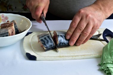 Uskumru balığının ve erkek ellerinin yakın plan görüntüsü balığı Chikorim bıçağıyla parçalara ayırır..