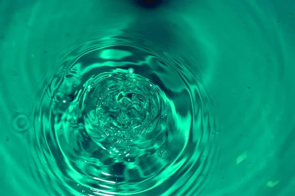 Un chorro de ondas circulares de una gota de agua que cae sobre la superficie de un líquido. — Foto de Stock