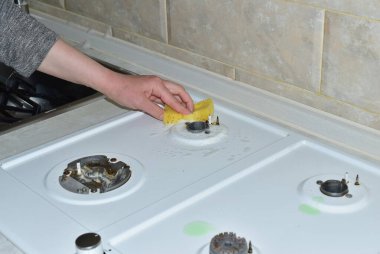 Bir kadın eli gaz sobasının yüzeyini süngerle temizler..