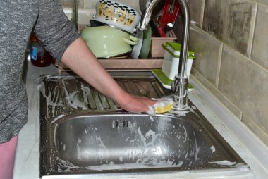 Bir kadın lavabonun metal yüzeyini havluyla yıkıyor..