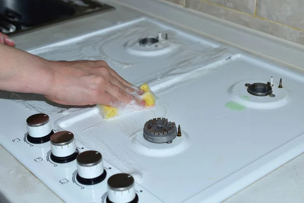 Una mujer limpia la superficie de una estufa de gas con una esponja. — Foto de Stock