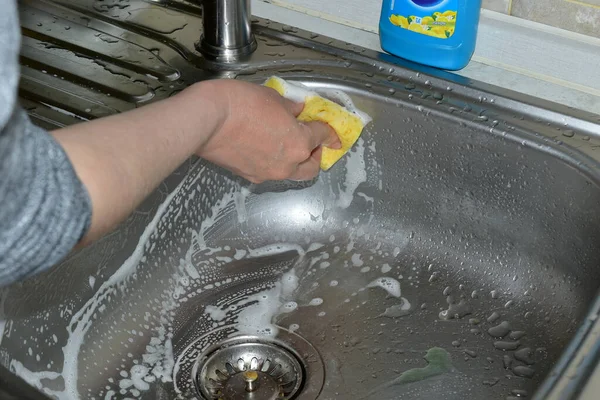Die Frau wäscht mit einem Waschlappen und Reinigungsmitteln die Oberfläche des Waschbeckens. — Stockfoto
