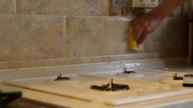 Bir kadın seramik bir fayansın yüzeyini gaz sobasının üzerine sünger ve deterjanla siliyor..