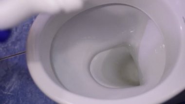 Ev sahibesi temizlik maddesini bir konteynırdan klozetin duvarlarına dairesel bir hareketle uyguluyor..