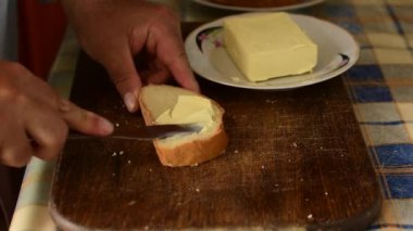 Bıçaklı bir adam buğday unundan yapılan ekmeğe tereyağı sürer..