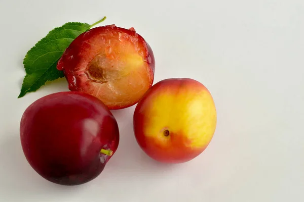 Zwei große Kirschpflaumen und eine Hälfte mit grünen Blättern liegen auf dem Tisch. — Stockfoto