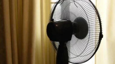 Video çalışan bir yelpazenin yakın çekimini gösteriyor, farklı yönlerdeki hava akımlarını yönlendiriyor..