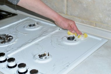 Bir kadın gaz sobasının yüzeyini yıkıyor..