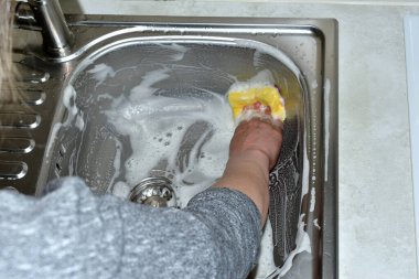 Bir kadın mutfakta bir süngerle lavaboyu yıkıyor..