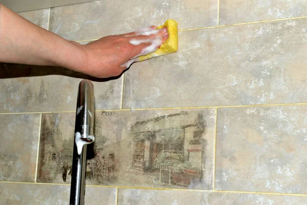 Una mujer lava azulejos de cerámica en la cocina con una esponja. — Foto de Stock