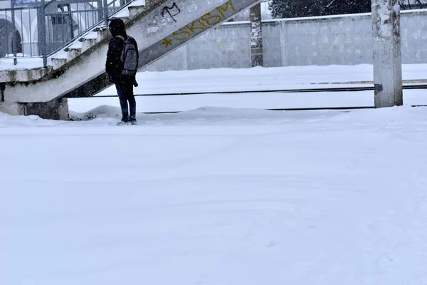 El invierno. Un hombre con una chaqueta con capucha está parado cerca del puente ferroviario.. — Foto de Stock