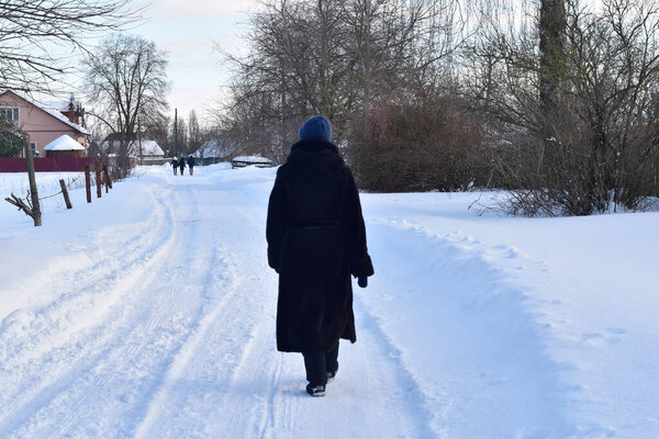 A woman in dark clothes walks along a road that is white with snow.