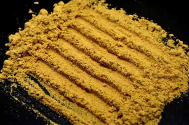 Dry ground mustard powder on black background.