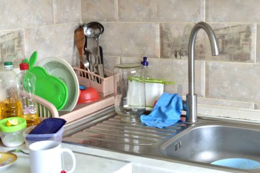 Lavabonun yanındaki mutfak masasında temiz tabaklar, tabaklar ve sebze yağı şişeleri var..