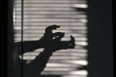 Duvardaki güneş ışığının ışığı ve gölgesi oyunu. Ellerin silueti, panjurların gölgesine yapışmış parmakları olan ellerin gölgeleri. Korku filmleri için bir zemin.