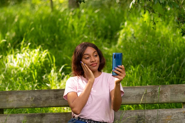 Genç siyah bir kadın, telefonuyla bir Ekim öğleden sonra parkta selfie çekiyor..